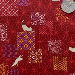 May include: Red fabric with a repeating pattern of squares and starbursts. The squares feature floral and geometric designs in white, purple, and yellow. Two white cat silhouettes are also present. A quarter is in the upper right corner.