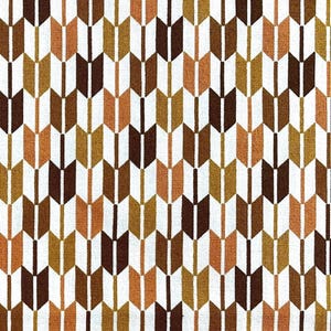 Op de afbeelding: Een witte stof met een herhalend patroon van bruine, oranje en gouden pijlen. De pijlen zijn gerangschikt in een chevron-patroon.