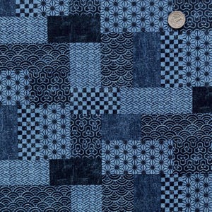 May include: A patchwork fabric with a variety of geometric patterns in shades of blue and navy. The design includes squares, circles, and starbursts. A quarter coin is placed on the fabric for scale.