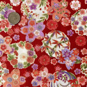 May include: Red fabric with a repeating pattern of gold and white flowers, leaves, and geometric shapes. The fabric has a subtle sheen and a textured surface.