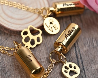 May include: Two gold necklaces with engraved paw print charms and small cylindrical pendants. The pendants are engraved with the names "Joy", "Arthur 01.01.2001", and "Thormade A750". One necklace also has a charm with the word "LOVE" engraved on it.