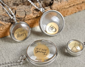 May include: Three silver necklaces with glass pendants. The pendants contain small gold discs with engraved text. The text on the discs reads "Luigi 2024 3/11", "Sweet? 2024 3/16", and a paw print inside a heart.