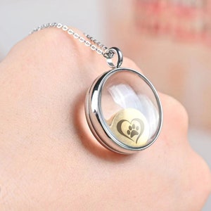 Pu&ograve; includere: Collana con catena d'argento e ciondolo rotondo in vetro. Il ciondolo contiene un cuore d'oro con un'impronta di zampa all'interno.