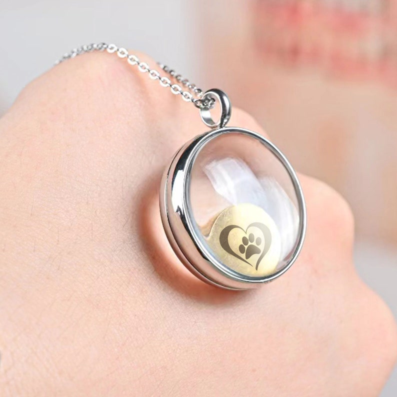 Pu&ograve; includere: Collana con catena d'argento e ciondolo rotondo in vetro. Il ciondolo contiene un cuore d'oro con un'impronta di zampa all'interno.