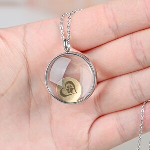 Pu&ograve; includere: Collana con catena d'argento con un ciondolo rotondo in vetro trasparente che contiene un cuore dorato con un'impronta di zampa all'interno.