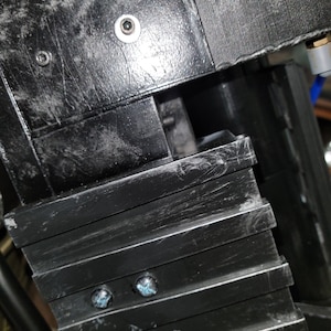 以下が含まれることがあります： 積み重ねられた長方形のプレートを持つ黒い金属製のオブジェクトのクローズアップ。オブジェクトの上部には小さな灰色のノブがあり、前面には2つの小さな青いネジがあります。