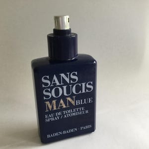 Könnte beinhalten: Eine marineblaue, rechteckige Parfümflasche mit einem silbernen Zerstäuber. Die Flasche trägt den weißen Schriftzug "SANS SOUCIS MAN BLUE" und "EAU DE TOILETTE SPRAY / ATOMISEUR" und "BADEN-BADEN - PARIS".