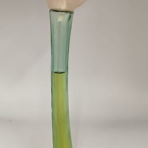 Könnte beinhalten: Ein Parfümflakon mit blütenförmigem Aufsatz. Die Flasche hat einen langen, gebogenen, grünen Stiel und eine hellrosa blütenförmige Kappe. Die Flüssigkeit im Inneren ist hellgelbgrün. Die Flasche steht vor weißem Hintergrund.