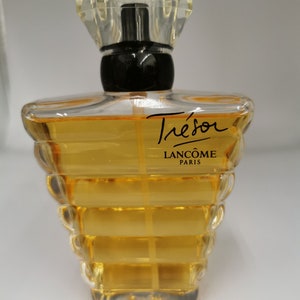 Könnte beinhalten: Ein klarer Glasparfümflakon mit facettiertem Verschluss und schwarzem Kragen. Die Flasche ist mit einer goldfarbenen Flüssigkeit gefüllt und trägt die Aufschrift "Trésor" und "Lancôme Paris".