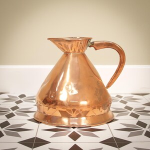 May include: A copper jug with a wide base and a flared spout. The jug has a hammered finish and a curved handle.