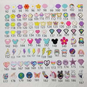 May include: A collection of decorative iron-on patches in various shapes and colors. Designs include flowers, crowns, butterflies, smiley faces, hearts, diamonds, and cartoon characters. Each patch is numbered for easy selection.