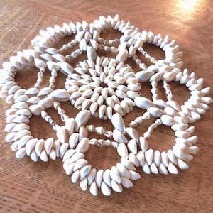 May include: A white seashell coaster with a circular design. The coaster is made of many small seashells that are woven together.