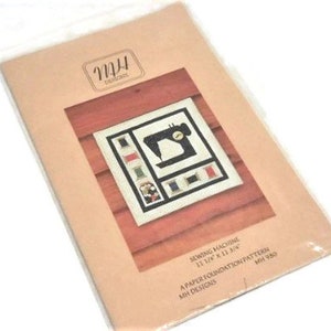 May include: A paper foundation pattern for a sewing machine cross stitch project. The pattern is titled "Sewing Machine" and measures 12 1/4 inches by 11 3/4 inches. The pattern is from MH Designs and is numbered MH 980.