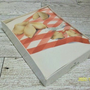 May include: A white card with a red and white checkered pattern. The card features a design of fortune cookies with the text "You are a gift to the world".