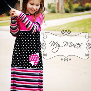 以下が含まれることがあります： ピンク、黒、白の模様のドレスを着た少女。髪には大きなピンクの花が飾られています。ドレスは水玉模様のスカートとストライプの袖が特徴です。黒い傘を持っています。