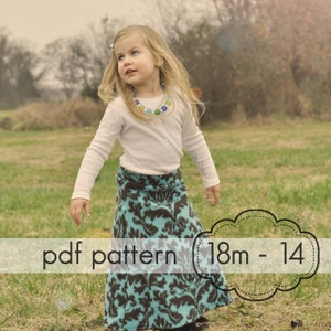 May include: A young girl wearing a long-sleeved white shirt and a teal and brown patterned skirt. The skirt has a floral design. The image includes the text "pdf pattern 18m - 14". She is wearing a necklace with colorful beads.
