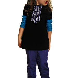 以下が含まれることがあります： 白と青の装飾トリムが付いた黒いチュニックと、青い長袖シャツを重ね着した子供用衣装。紫色のパンツと黒いメリージェーンシューズが含まれています。