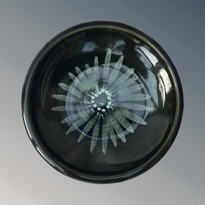 May include: A black ceramic bowl with a white, starburst design. The bowl has a glossy finish.