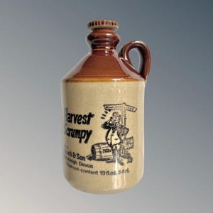 Könnte beinhalten: Brauner und beigefarbener Keramikkrug mit Henkel und Verschluss. Der Krug trägt die Aufschrift "Harvest Scrumpy" und eine Illustration einer Person mit einem Fass. Mindestinhalt des Kruges: 54 cl.