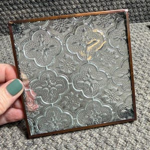 Puede incluir: Panel de vidrio cuadrado con un patrón floral y de cuatro hojas, enmarcado en metal marrón oscuro. El diseño de vidrio transparente presenta flores en relieve y formas de trébol de cuatro hojas.