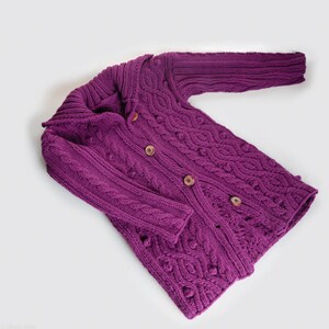 Könnte beinhalten: Ein lilafarbener Strickcardigan mit Zopfmuster und Knopfleiste.