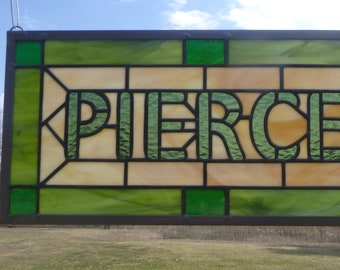 May include: A stained glass window with the name "PIERCE" in green letters on a background of green, beige, and white glass.