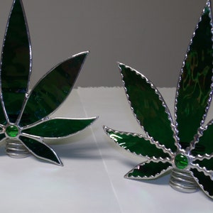 May include: Two green stained glass marijuana leaf ornaments with silver accents. Each ornament has a green jewel in the center.