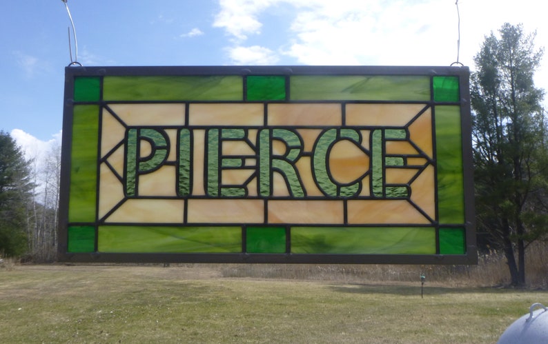 May include: A stained glass window with a green and brown frame. The window features the word 'PIERCE' in green lettering on a light brown background.
