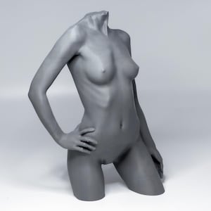 Peut inclure: Une sculpture de torse grise sans tête, avec un bras plié au coude et la main sur la hanche. L'autre bras est tendu. La sculpture est à genoux sur un genou. Le fond est blanc uni.