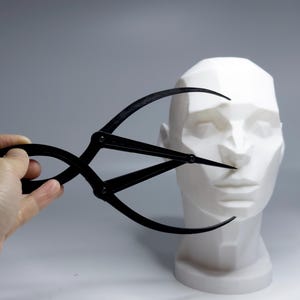 Peut inclure: Un outil de mesure en plastique noir, également appelé diviseur proportionnel, est utilisé pour mesurer les proportions d'un buste en plâtre blanc d'un visage humain.