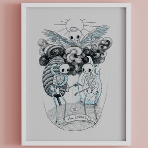 May include: A framed art print featuring a black and white illustration of skeletons. The artwork depicts two skeletons holding hands, with a cloud and sun design above them. The text "The Lovers" is at the bottom.