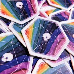 May include: A stack of colorful hexagonal stickers with a rainbow design and a white skull in the center. The stickers are printed on white paper and have a glossy finish.