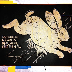 May include: A black and white print featuring a running rabbit with the words "NO BORDERS NO WALLS ABOLISH ICE FREE THEM ALL". The rabbit is cream-colored with black spots and is set against a black background.