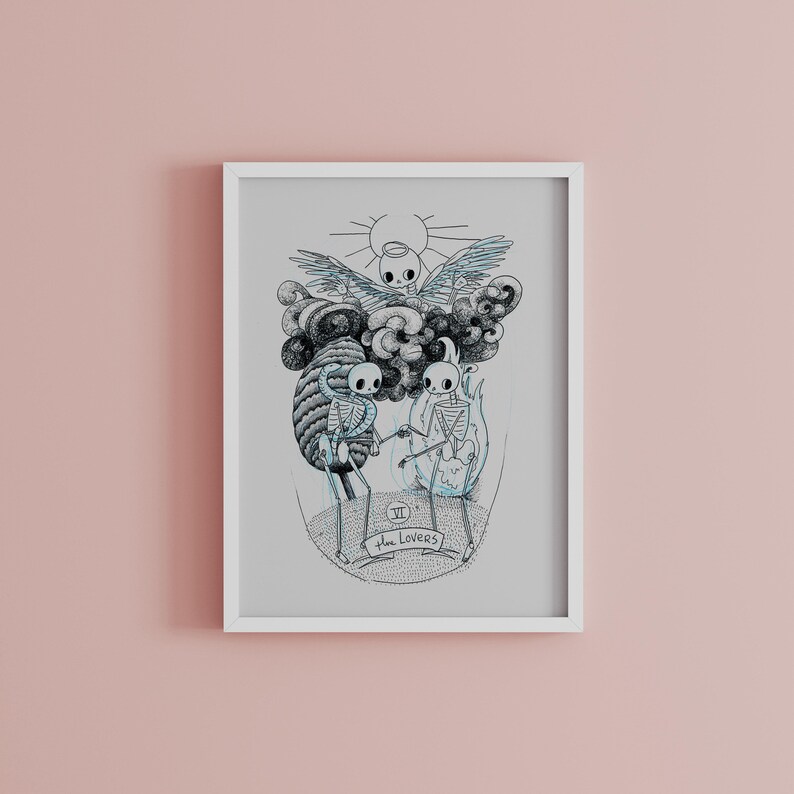 May include: A framed art print featuring a black and white illustration of skeletons. The artwork depicts two skeletons holding hands, with a cloud and sun design above them. The text "The Lovers" is at the bottom.