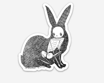 以下が含まれることがあります： 黒と白の線画で描かれた、中に骨格が入ったウサギ。ウサギは耳を立てて目を閉じ、座っている。画像の下部には「CAT ROCKETSHIP」というテキストが書かれている。