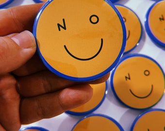 Blue pinback button with a smiley face on it that says NO where the eyes should be. A funny gift for a teen or millennial. No thanks pin.