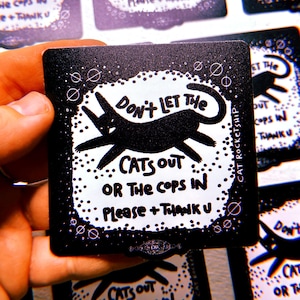 Puede incluir: Pegatina en blanco y negro con una silueta de gato negro y el texto "No dejes que los gatos salgan o la policía entre. Por favor + Gracias." La pegatina tiene un fondo negro con puntos blancos.