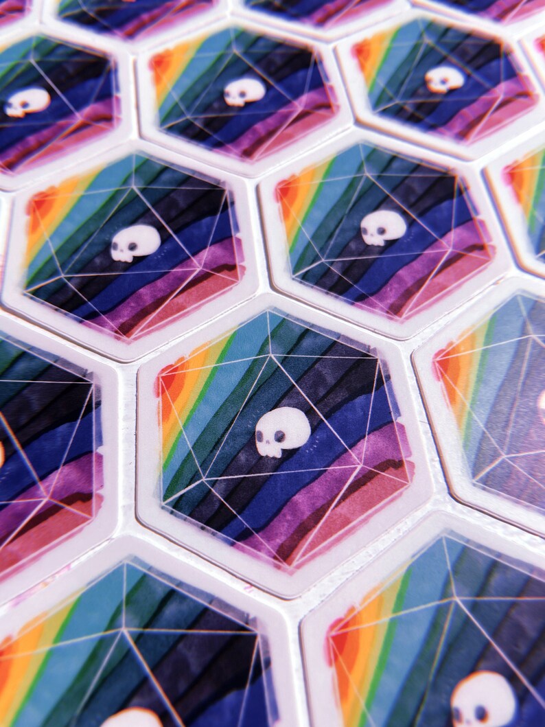 Puede incluir: Primer plano de fichas de juego hexagonales con un dise&ntilde;o de arco&iacute;ris y una calavera blanca en el centro de cada ficha.