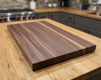 May include: A rectangular, dark walnut cutting board with a smooth, polished surface. The wood grain is visible, showcasing natural patterns. The board is placed on a light-colored wooden countertop, suggesting a kitchen setting. This item is suitable for food preparation.