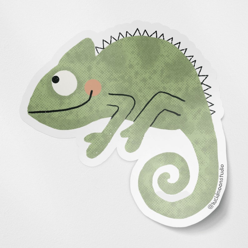 A photo of a die-cut glossy vinyl sticker featuring a cute hand-drawn green chameleon smiling.