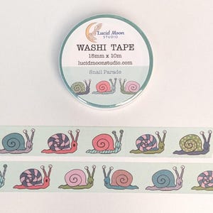 A roll of packaged washi tape by lucidmoonstudio.com with two strips of tape decorated with hand-drawn snails in shades of pink, blue, purple, and green making different facial expressions on a pale aqua background.
