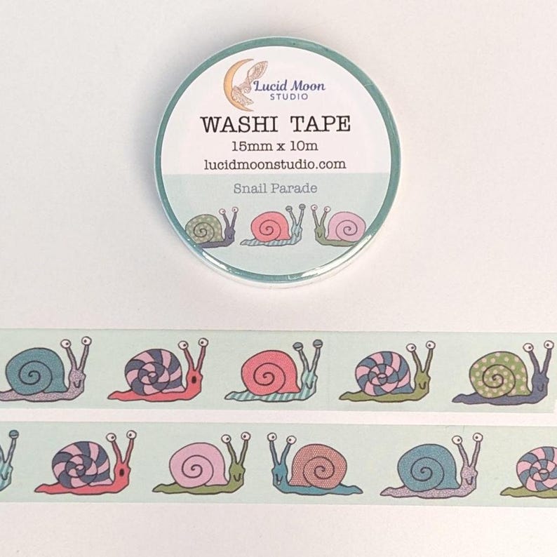 A roll of packaged washi tape by lucidmoonstudio.com with two strips of tape decorated with hand-drawn snails in shades of pink, blue, purple, and green making different facial expressions on a pale aqua background.