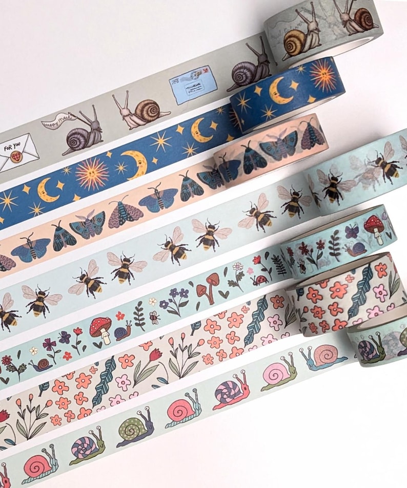 A collection of decorative washi tape rolls featuring various nature-inspired designs. The tapes showcase illustrations of snails, bees, butterflies, flowers, and celestial elements like moons and stars. The color palette includes soft blues, greens, and pinks.