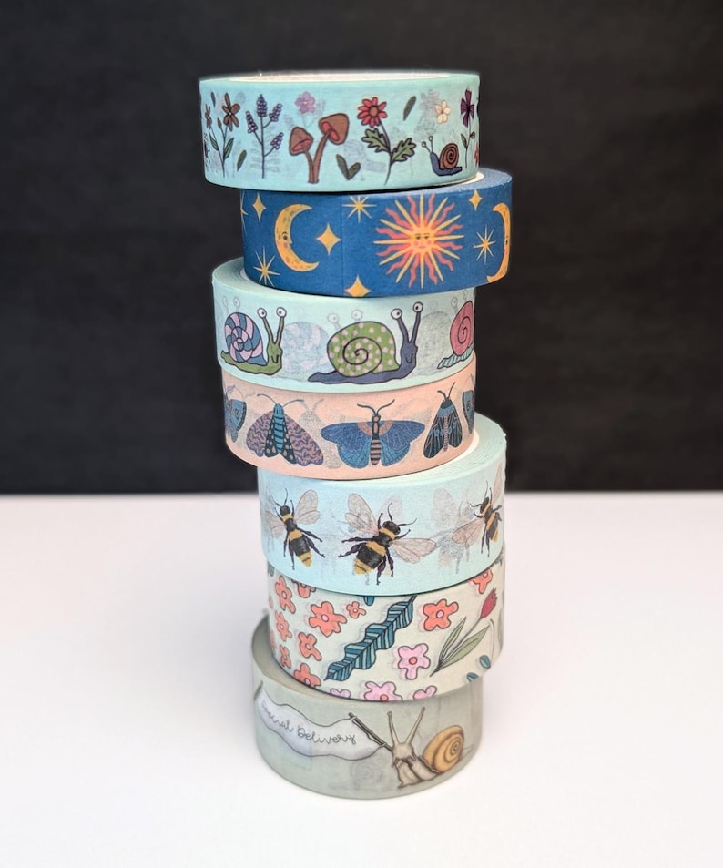 A stack of decorative washi tape rolls with various nature-themed designs. The rolls feature illustrations of flowers, mushrooms, bees, snails, moths, and celestial bodies in shades of blue, pink, and green. The bottom roll features snails holding a banner with the text "Special Delivery".