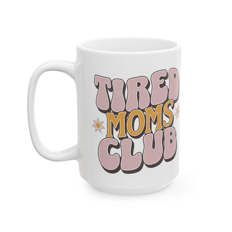 May include: White ceramic mug with the text "TIRED MOMS CLUB" in a retro font. The text is in pink and orange with a shadow effect, and there are star accents. The mug has a large handle.