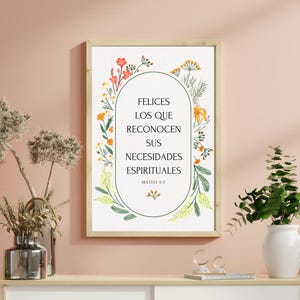 May include: A framed print with the text "FELICES LOS QUE RECONOCEN SUS NECESIDADES ESPIRITUALES" in a floral design. The print is displayed on a white cabinet with plants and decorative lighting.