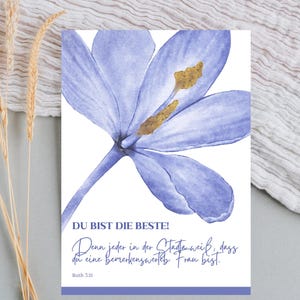 May include: A watercolor print featuring a large, light purple flower with a golden center. The print includes German text that reads "DU BIST DIE BESTE!" and a quote from Ruth 3:11. The background is white.