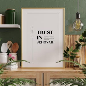 Puede incluir: Una impresión enmarcada con las palabras "TRUST IN JEHOVAH" en texto negro. La impresión está en un marco dorado y se muestra en un mueble de madera. El fondo incluye una pared verde, un estante con frascos y plantas decorativas.