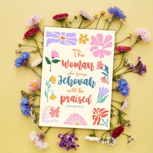 Könnte beinhalten: Eine cremefarbene Karte mit dem Text „Die Frau, die Jehova fürchtet, wird gelobt werden“, umgeben von farbenfrohen Blumenillustrationen. Die Karte wird von einer Vielzahl frischer Blumen auf gelbem Hintergrund umrahmt.