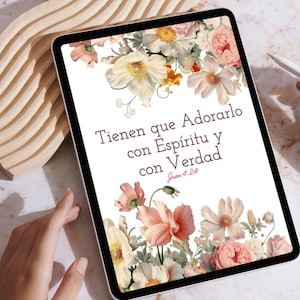 May include: A digital tablet displays text in Spanish, "Tienen que Adorarlo con Espíritu y con Verdad Juan 4:24," surrounded by a floral border of pink, peach, and white flowers. The tablet is held by a person.